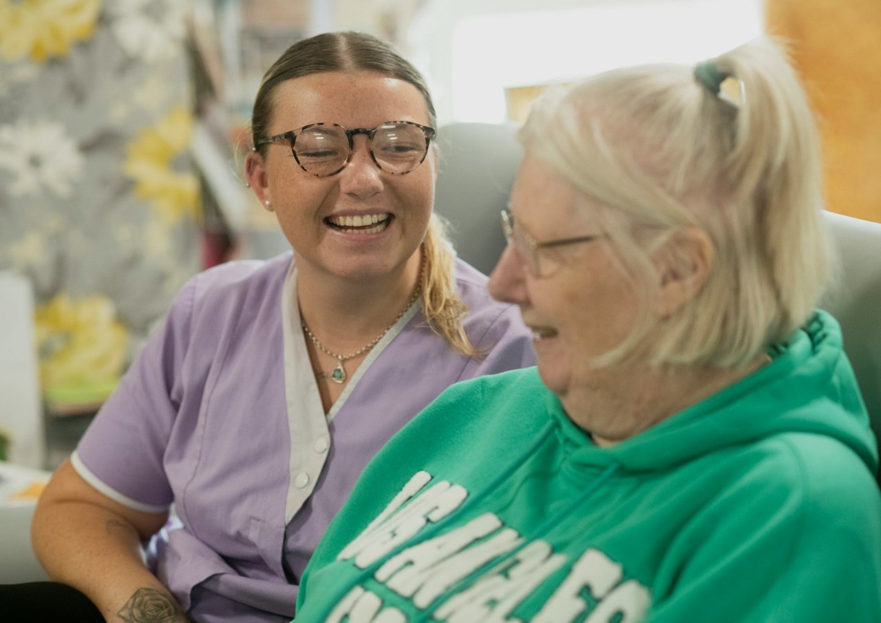 A smiling carer sitting with an older woman