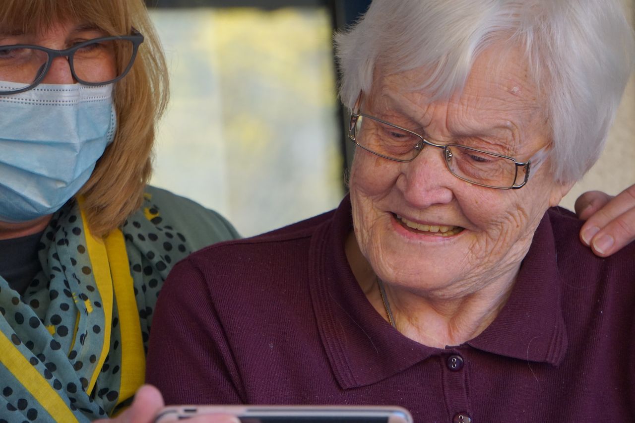 A carer and a smiling older woman looking at a tablet together